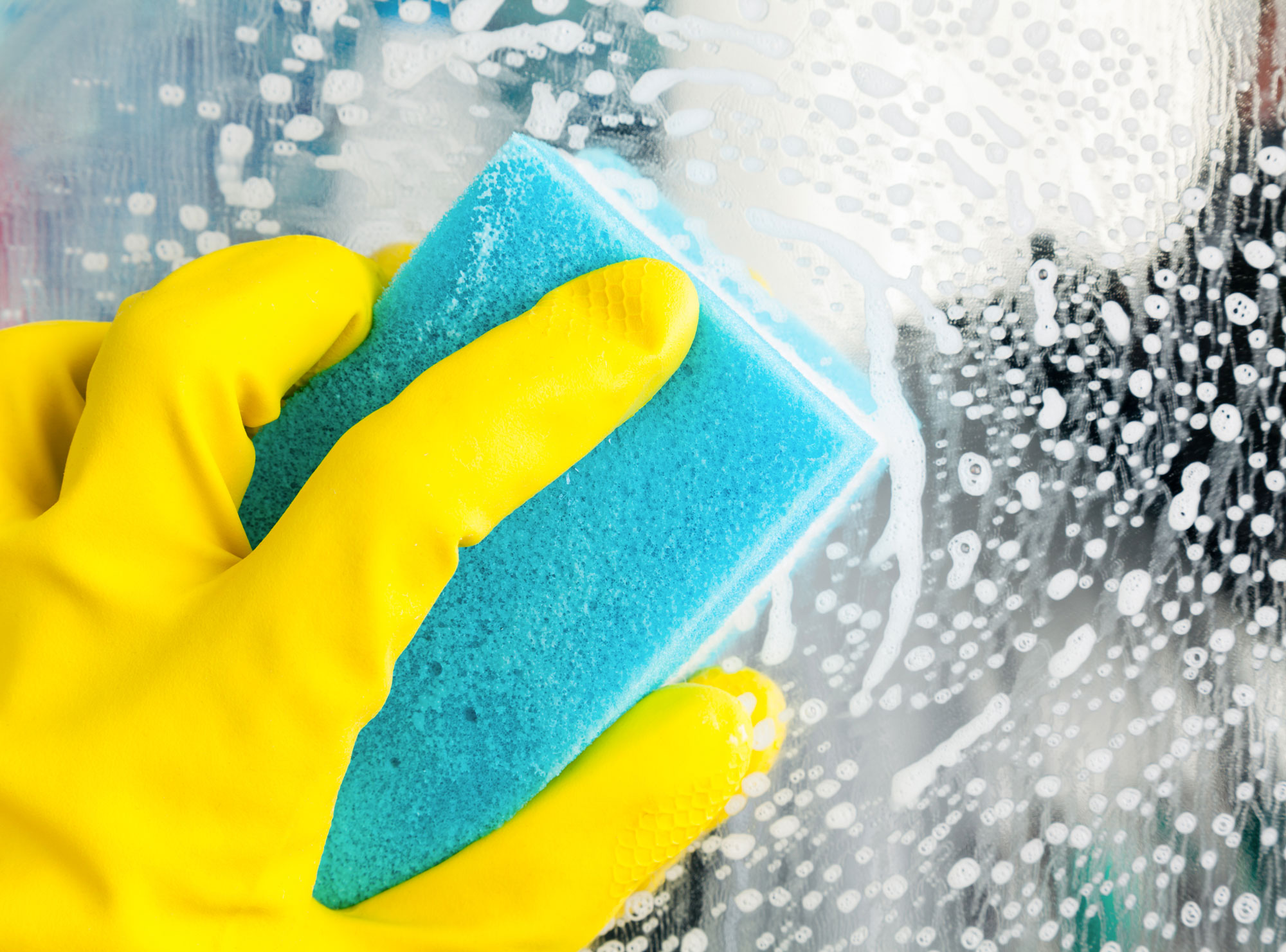 Someone is wearing a yellow glove and holding a blue sponge while scrubbing a shower door.