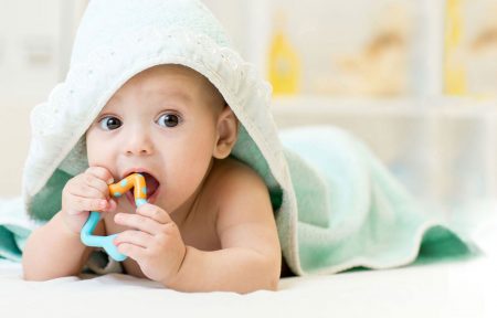 Mit einer Decke zugedecktes Baby, das auf dem Bauch liegend ein Spielzeug mit dem Mund entdeckt
