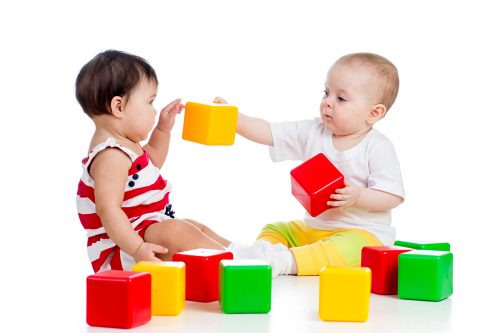 two babies playing together with colored blocks